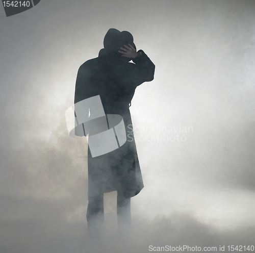 Image of Woman wearing trench coat and standing in fog