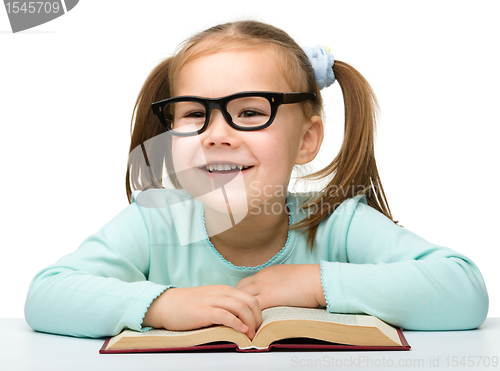 Image of Little girl reads a book while wearing glasses