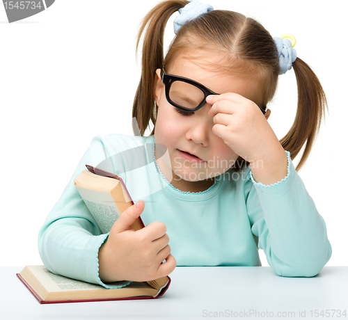 Image of Little girl reads a book while wearing glasses