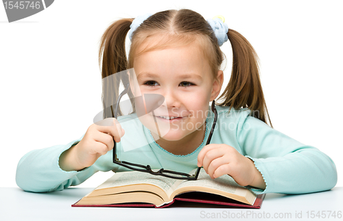 Image of Little girl reads a book while wearing glasses
