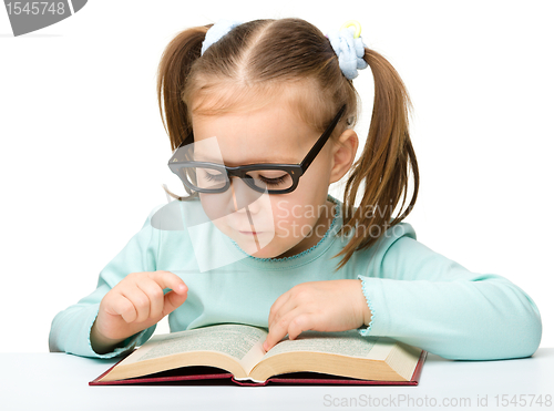 Image of Little girl reads a book while wearing glasses