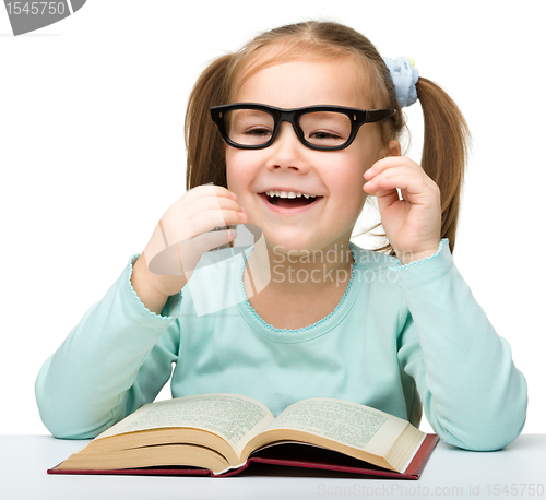Image of Little girl reads a book while wearing glasses