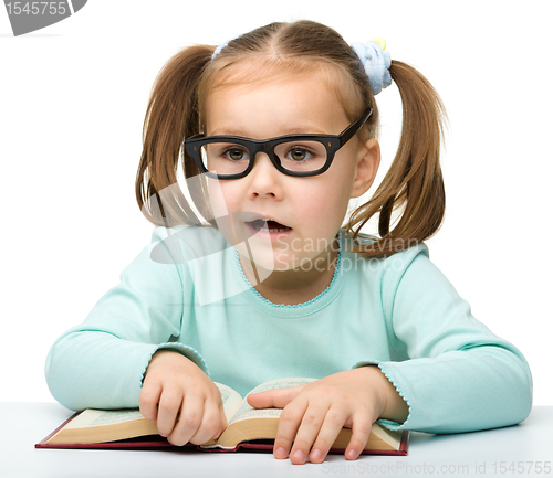 Image of Little girl reads a book while wearing glasses