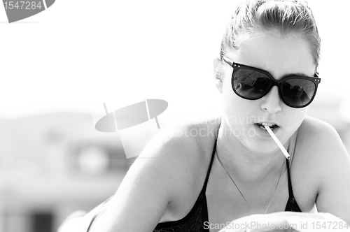 Image of Young woman in swimsuit starting to smoke on the beach