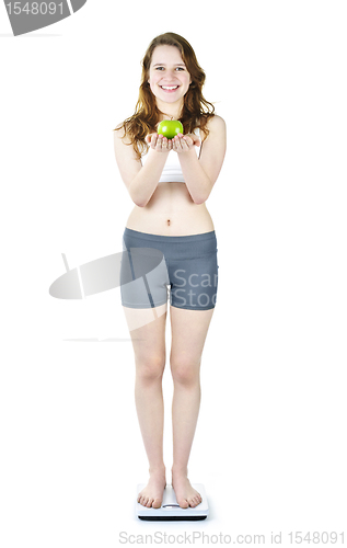 Image of Young smiling girl on bathroom scale holding apple