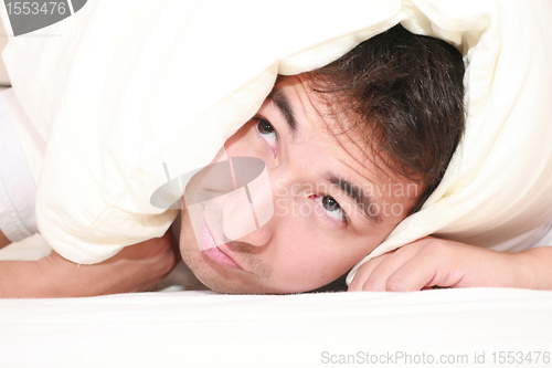 Image of Man trying to sleep with a pillow over his head and close to wake up time