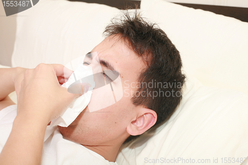 Image of Sick man blowing his nose lying on his bed at morning