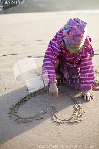 Image of Girl drawing a heart in sand