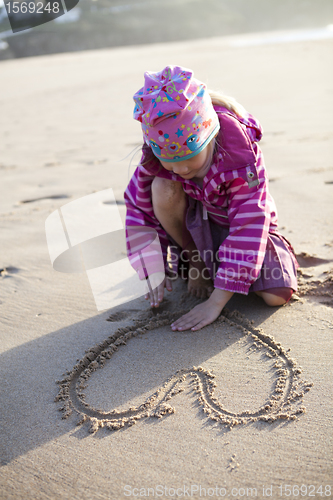 Image of Girl drawing a heart in sand