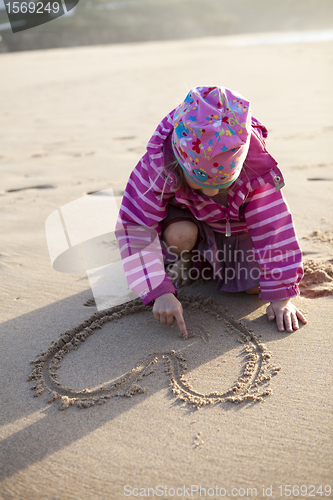 Image of Girl drawing a heart in sand