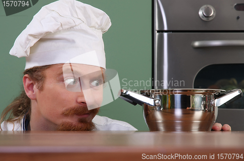 Image of Funny young chef strange looking at pot