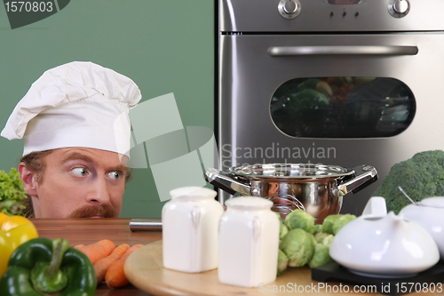 Image of Funny young chef strange looking at pot