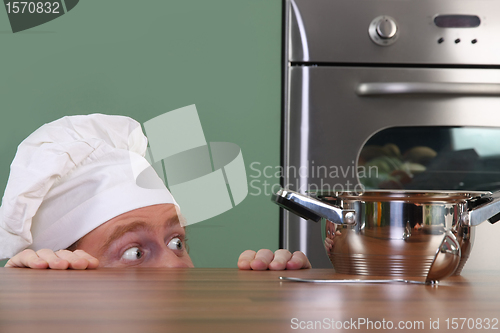 Image of Funny young chef strange looking at pot