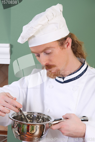 Image of young Chef tasting food with a tablespoon 