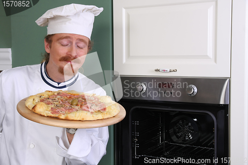 Image of Young chef smelling italian pizza in kitchen