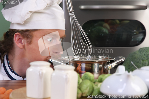 Image of Funny young chef strange looking at pot