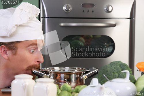 Image of Funny young chef strange looking at pot