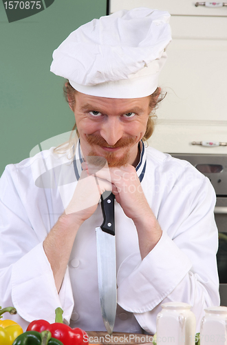Image of Funny young chef with a knife in kitchen