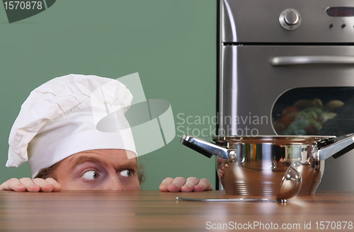 Image of Funny young chef strange looking at pot