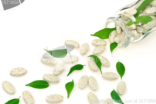 Image of Herbal supplement pills and fresh leaves  spilling out of bottle