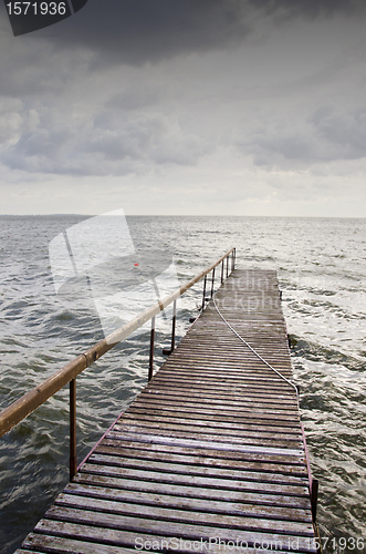 Image of Wooden bridge on wavy lake. Dark sky before storm 