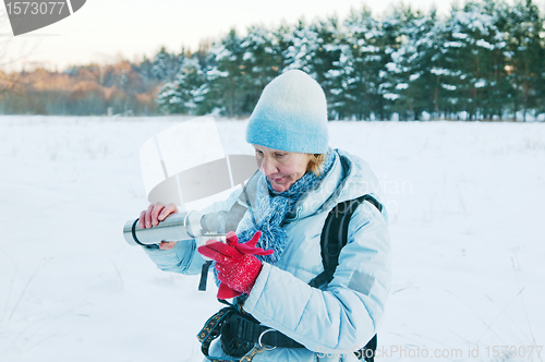 Image of The woman pours from a thermos tea, in winter on walk