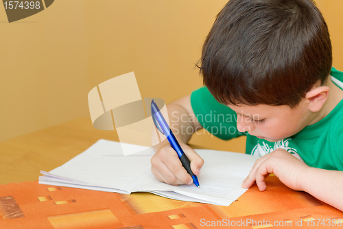 Image of school boy writting homework in workbook