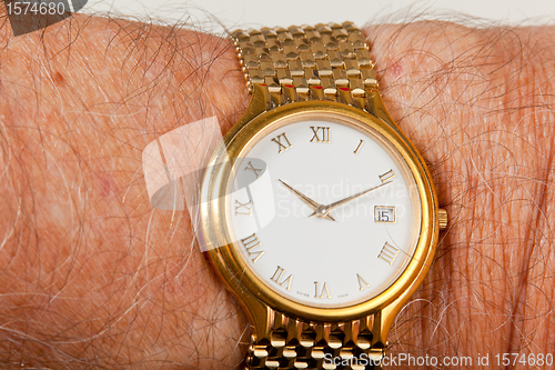 Image of Gold watch with white face on hairy wrist