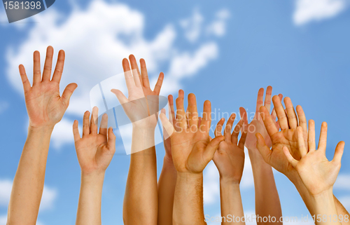 Image of Hands raised up in air across blue sky 