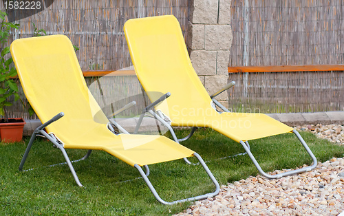 Image of Two empty yellow sun loungers on a garden 