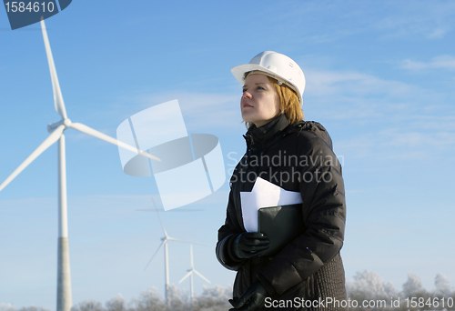Image of Young architect-woman wearing winter cloth standing against wind turbines