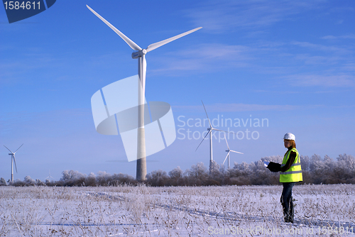 Image of Young architect-woman wearing winter cloth standing against wind turbines