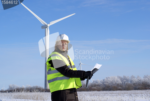 Image of Young architect-woman wearing winter cloth standing against wind turbines