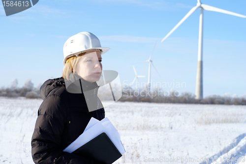 Image of Young architect-woman wearing winter cloth standing against wind turbines