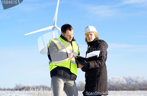 Image of Young architect-woman wearing winter cloth and engineer standing against wind turbines