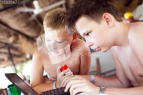 Image of Two boys play a laptop on rest in a bar on a beach