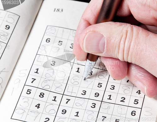 Image of Man hand holding pencil on sudoku puzzle