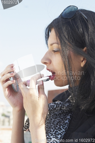 Image of beautiful woman paints her lips with lipstick
