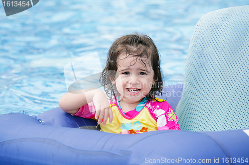 Image of Baby girl having fun on a blue float into a tropical swimming po