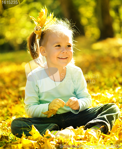 Image of Cute little girl is playing with leaves in park