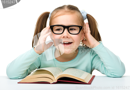 Image of Little girl reads a book while wearing glasses