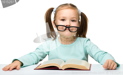 Image of Little girl reads a book while wearing glasses