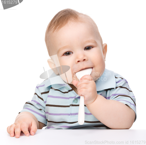Image of Little boy is biting a spoon sitting at table