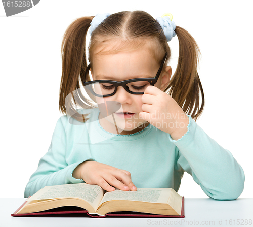 Image of Little girl reads a book while wearing glasses