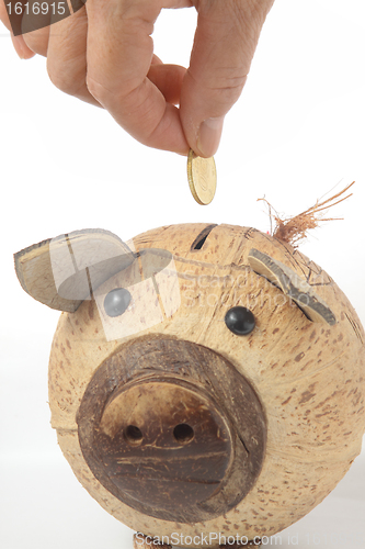 Image of Saving, male hand putting a coin into piggy bank. 