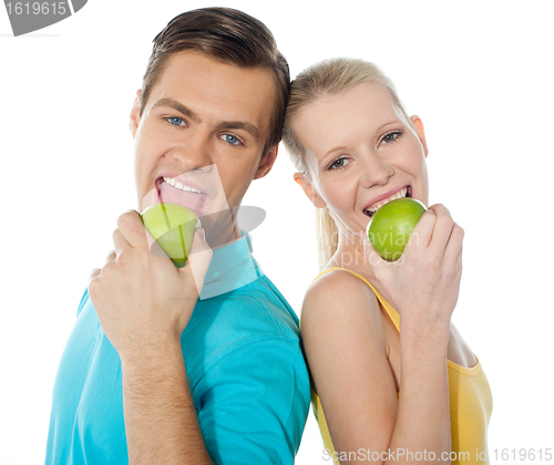 Image of Young couple posing back to back with green apples