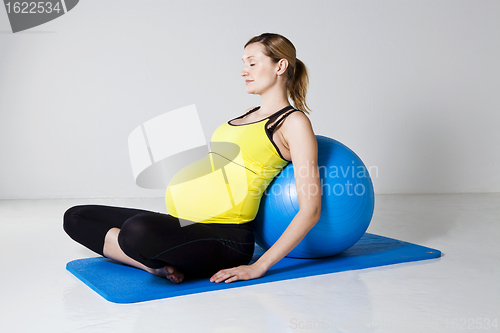 Image of Pregnant woman relaxing against fitness ball