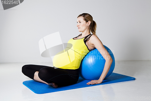 Image of Pregnant woman relaxing against fitness ball