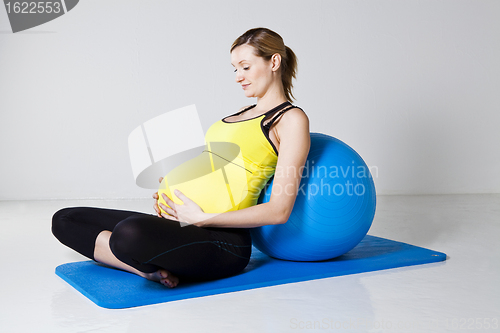 Image of Pregnant woman relaxing against fitness ball