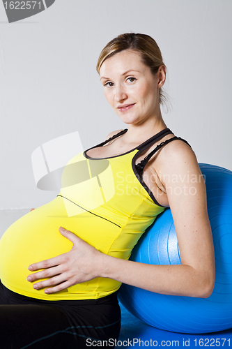 Image of Pregnant woman relaxing against fitness ball